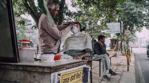 People sitting on table by street against trees