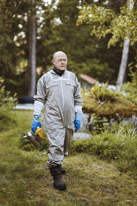 Full length of beekeeper holding smoker while walking on field