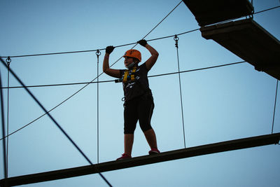 Low angle view of girl walking on rope against sky