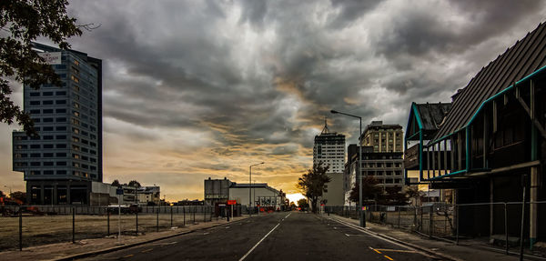 Road passing through city against cloudy sky