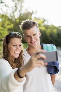 Happy young couple taking self portrait through mobile phone outdoors