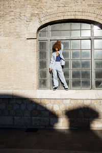 Young woman standing on window sill during sunny day