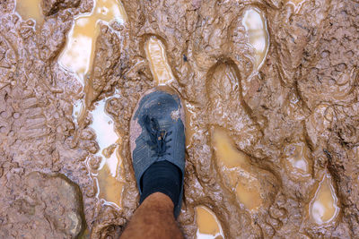 View from above on pair of trekking shoes in a mud, hiking boots stuck in mud.