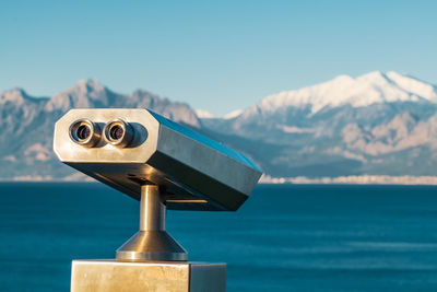 Close-up of coin-operated binoculars by sea against sky