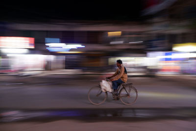 Rear view of man riding bicycles on street at night