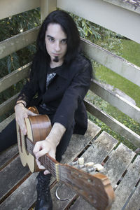 High angle portrait of hipster with guitar sitting at balcony