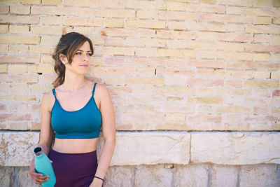 Young woman standing against brick wall