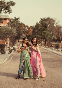 Portrait of two young women standing on road against trees