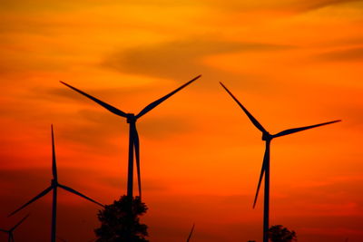 Silhouette of wind turbine against orange sky