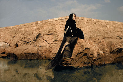 Young woman sitting on rock against sky