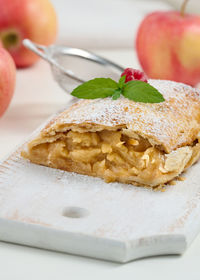 Baked strudel with apples sprinkled with powdered sugar on a white wooden board, delicious dessert