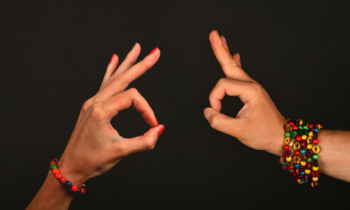 Cropped hands on man and woman making ok sign against black background