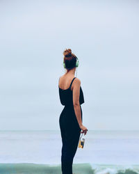 Rear view of woman standing on beach against clear sky