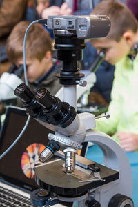 Close-up of microscope with boys experimenting in background