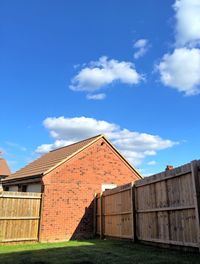 Wooden fence by house on field against sky