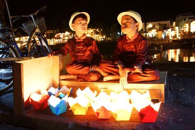 Portrait of happy friends sitting on illuminated at night
