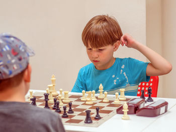 Eight-year-old boy plays chess at a table with an unrecognizable opponent.