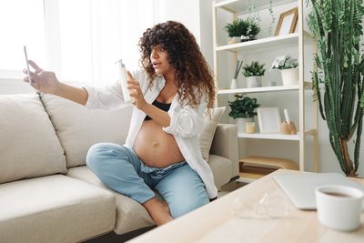 Young woman using mobile phone while sitting on sofa at home