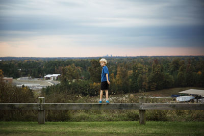 Boy standing on wooden fence against trees