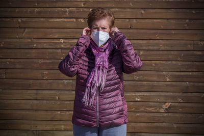 Senior woman with medical mask on face in prevention of coronavirus with wall background