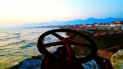 Bicycle by sea against sky during sunset