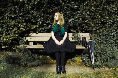 Young woman sitting on bench against tree