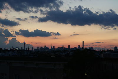 Silhouette city against cloudy sky during sunset