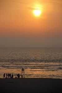 Silhouette people standing on beach against orange sky