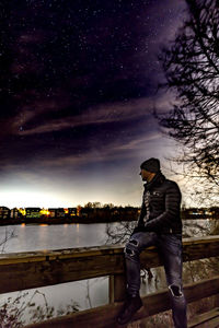 Man sitting by tree against sky at night