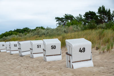 Hooded chairs on sand at beach against sky