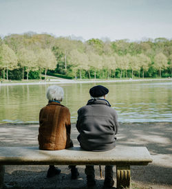 Rear view of couple sitting at lakeshore against sky