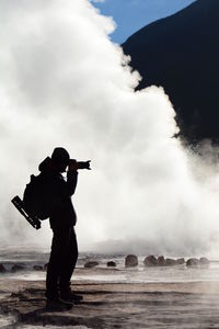 Silhouette photographer standing by splashing sea wave in forest