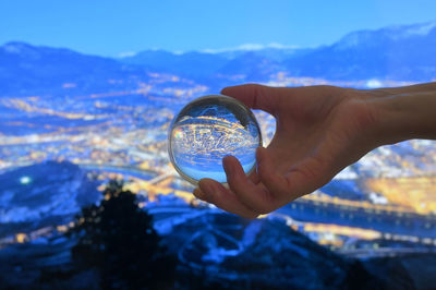 Midsection of person holding crystal ball against sky