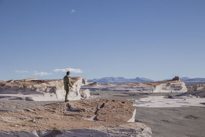 Rear view of man standing on rock formations against clear sky