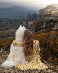 Rear view of woman sitting on rock looking at mountain