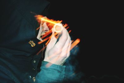 Midsection of woman holding fire against black background