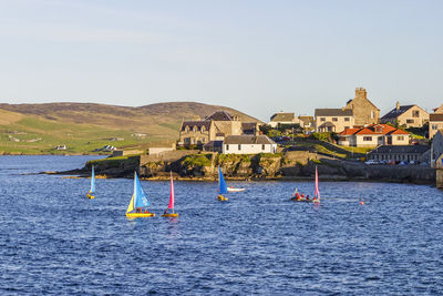 Sailboats in sea by buildings against clear sky