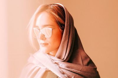 Close-up of beautiful woman in sunglasses and scarf against wall
