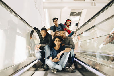 Portrait of confident male friends on moving walkway in shopping mall