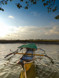 Fishing boat moored in lake against sky during sunset