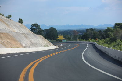 Empty road by trees against sky