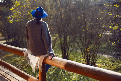 Village woman in a blue hat sits rear at a wooden house in autumn