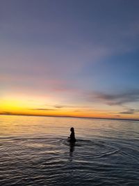 Silhouette person on sea against sky during sunset