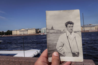 Cropped image of hand holding photograph against sea