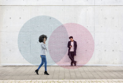 Women standing on footpath against wall