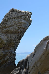 Low angle view of rock formation by sea against clear sky