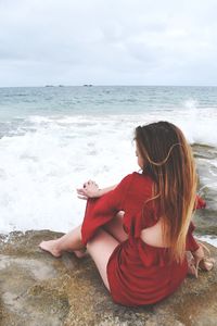 Woman sitting on beach looking at sea against sky