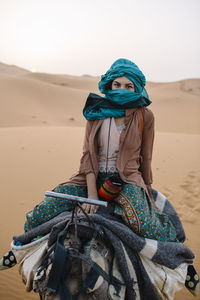 Portrait of woman wearing turban while sitting on camel at desert