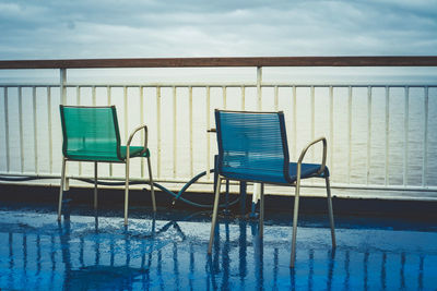 Empty chairs on pier by sea against cloudy sky