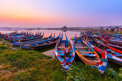 Fishing boats moored at riverbank against sky during sunset